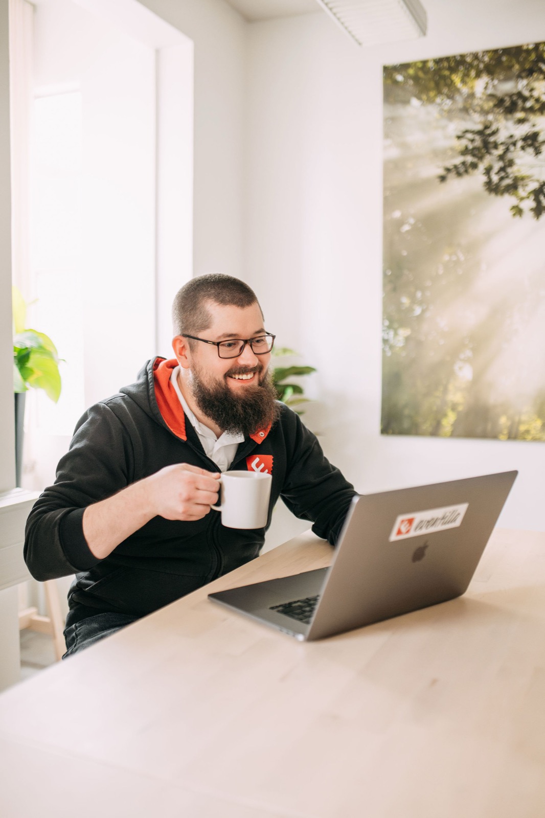 A CompetenceFlow team member smiling at a laptop with a coffee mug in the bright Oulu office in Finland