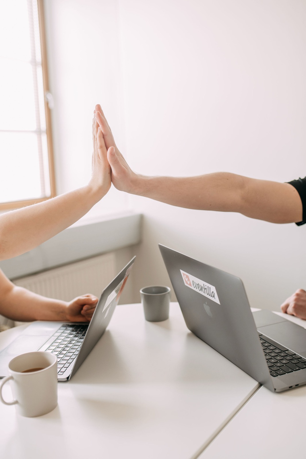 Two CompetenceFlow colleagues high-fiving over their laptops in the Oulu office in Finland