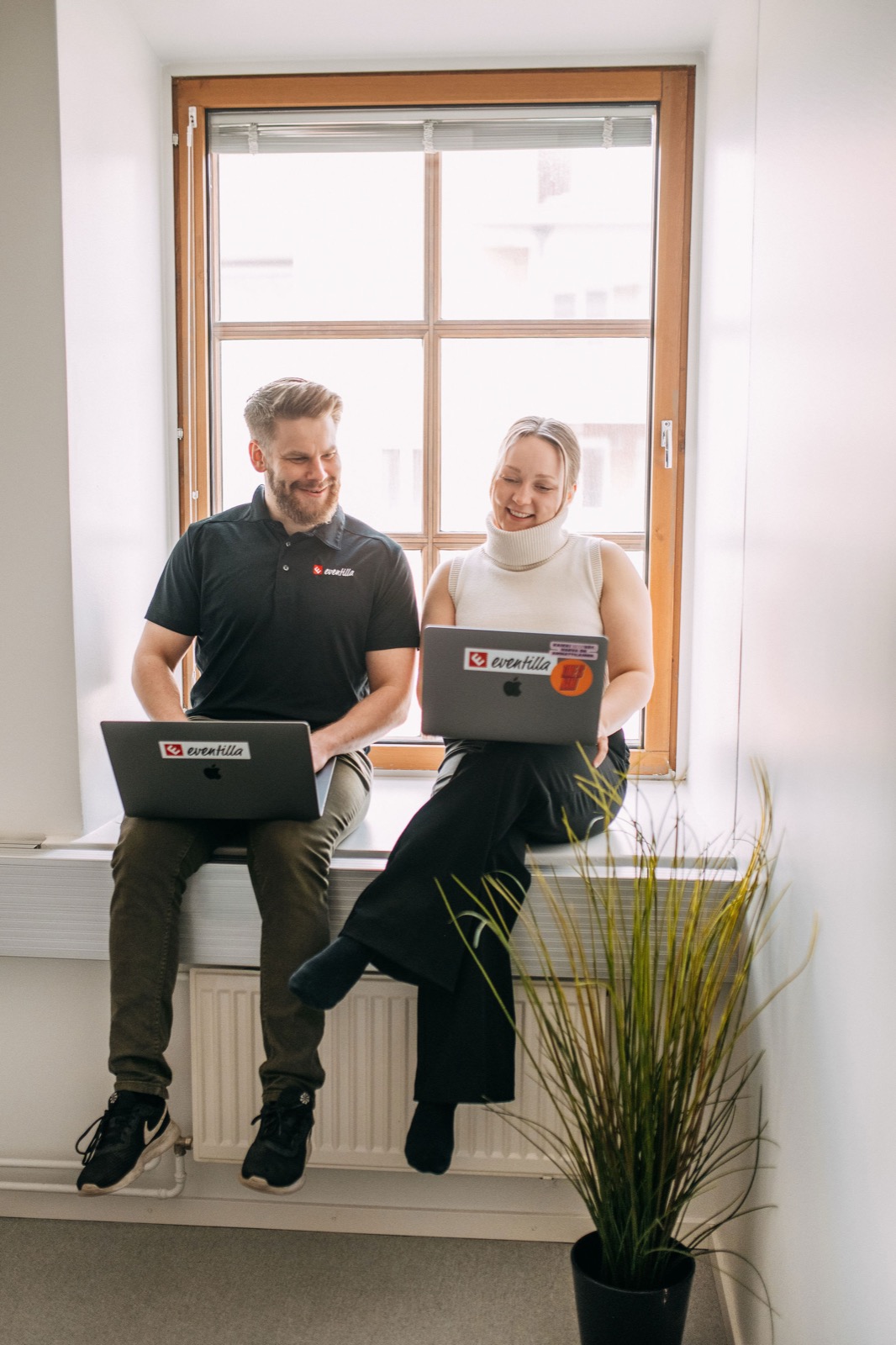 Two members of the CompetenceFlow team working on laptops by a bright window at the office in Oulu, Finland